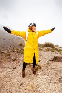 A hiker in a bright yellow raincoat embraces the rainy weather while trekking on a rugged mountain