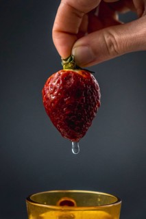 A water wet strawberry held by a woman's hand with black background