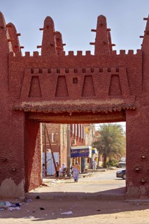 Red clay gate with traditional architecture in a sunny African town, palm trees in the background,