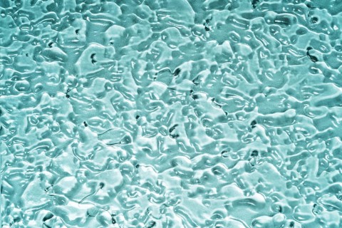 Top view of transparent gel smears covering a blue glass surface, creating a textured and abstract