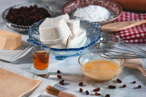 Baking ingredients in preparation, curd cheese, sultanas, sugar and bowl with egg mixture and a