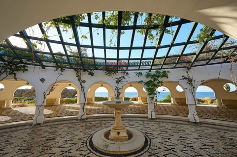 Bright courtyard with cobblestones and a central fountain, surrounded by white décor and sea views,