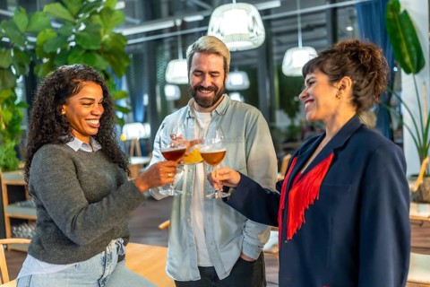 Multi-ethnic three happy friends toasting standing on a night bar terrace celebrating