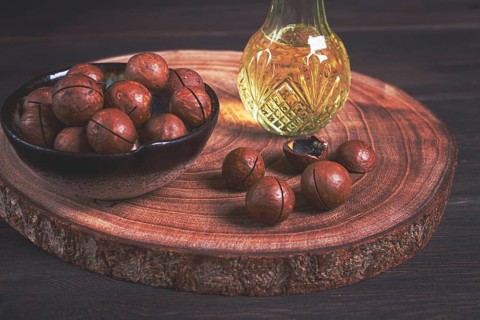 Bottle of macadamia oil, on a wooden board, with macadamia nuts, wooden background, selective