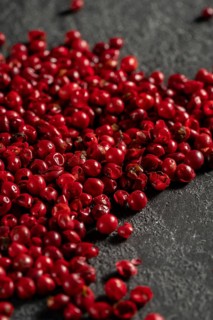 A close-up view of vibrant red peppercorns heaped on a textured dark slate surface, highlighting