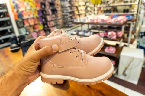 A person is holding a pair of pink shoes. The shoes are on display in a store