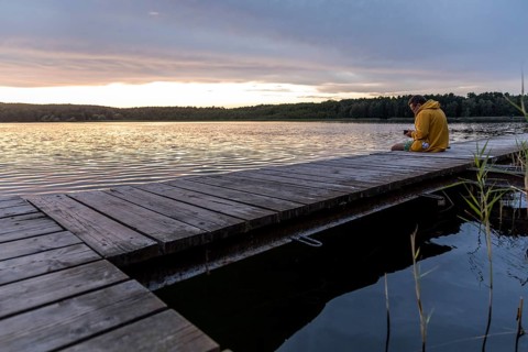 Man sitting on the bathing jetty and looking at his mobile phone, evening mood at the Großer