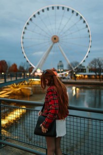 Back view of unrecognizable woman with red hair and a plaid jacket gazing at the illuminated Ferris