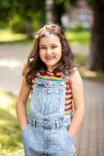 A cheerful little girl with long hair adorned with chamomile flowers smiles warmly at the camera.
