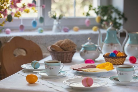 Breakfast table with Easter eggs, pastries and cold plate in front of decorated window