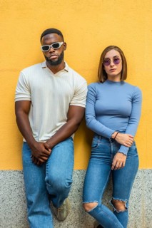 Vertical photo of two stylish multiracial people in casual denim clothes and sunglasses leaning on