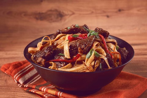 Udon noodles with beef in Mongolian style, with green onions and vegetables, served in a black