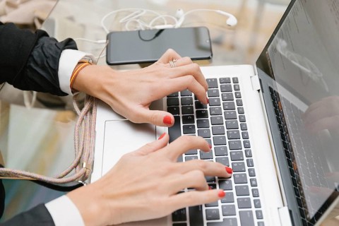 Busy woman working with laptop at home. There is a smartphone and headphones nearby. The image is