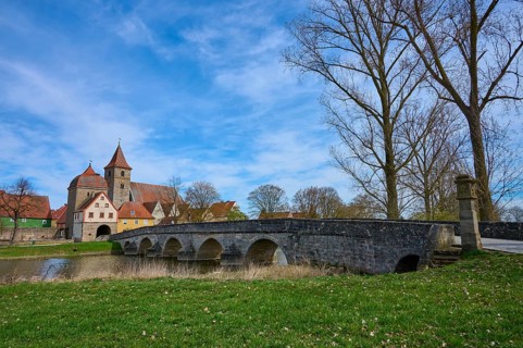 Stone bridge crosses river with view of an idyllic village with church and trees, spring, Ornbau,