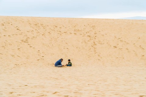 Father and child enjoy building sandcastles on an endless sandy desert under a cloudy sky. The