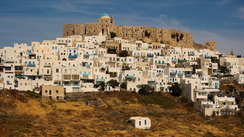 A historic fortress above a cluster of white houses and dry grass, Querini Castle, Chora,