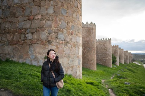 An Asian female tourist strolls along Avila's ancient medieval walls. The scene captures cultural