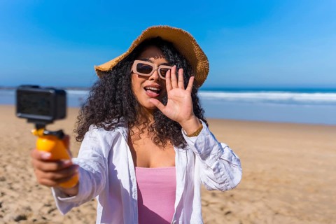 Young woman creating content for social media with an action camera on a sunny beach, sharing her