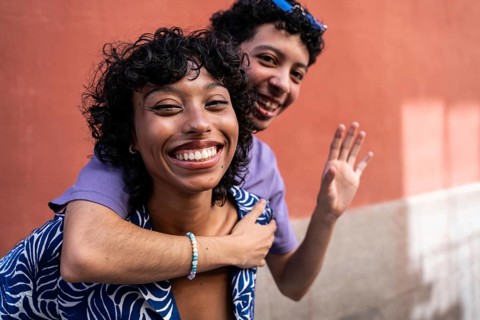 A happy multiethnic LGBTQ+ couple embraces and smiles against a vibrant outdoor backdrop. Their