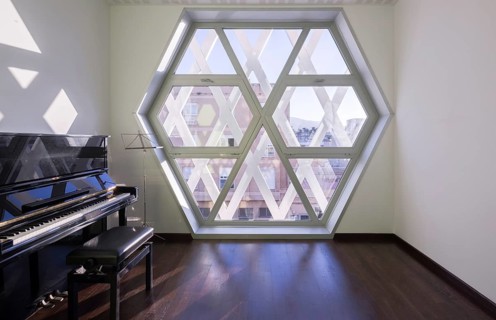 A modern auditorium room features a sleek black piano, a unique hexagonal window providing natural