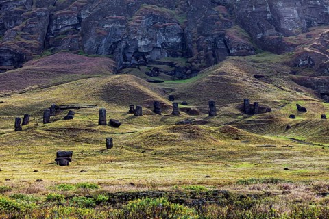 Several moai are spread over a gently rolling landscape under rocks, the moai statues on Easter