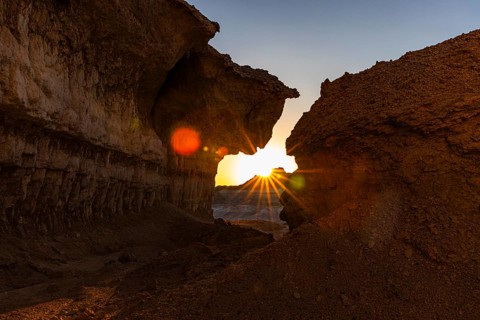 The morning sun shines through a striking rock formation in the Huqf stone desert, Arabian