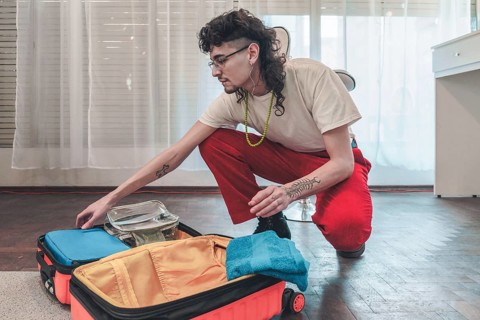Young stylish man is carefully packing his suitcase, organizing clothes, accessories, and