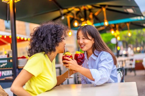 Romantic lesbian couple drinking cocktail together in an outdoor terrace enjoying summer in the