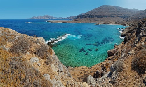 Panoramic views of a rocky coastline with clear turquoise waters and distant mountains under a