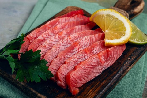 Chum salmon, cold smoked, sliced, on a cutting board, with lemon and parsley, top view, close-up,