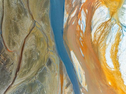 Top view of a vividly colored river meandering through diverse textured terrains, captured by a