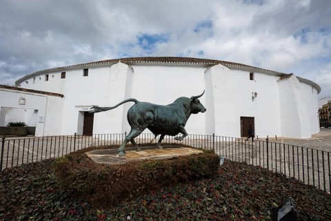 The white exterior of the Plaza de Toros de Ronda with a bronze bull statue in the foreground,