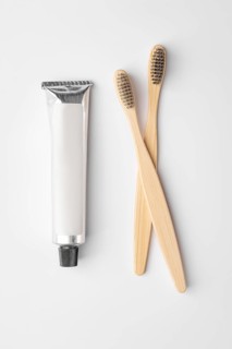 Top view of two bamboo toothbrushes with brown bristles and a metallic toothpaste tube are placed
