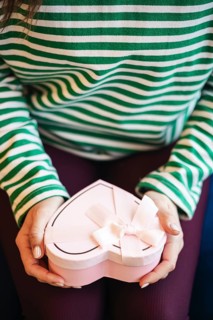 Cropped unrecognizable woman at a cafe holding a heart-shaped gift box decorated with a white
