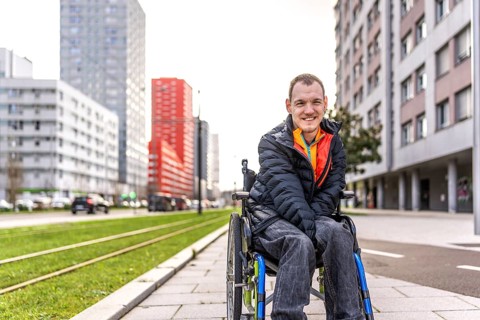 Young man with disability sitting in his wheelchair, smiling and enjoying a day out in an