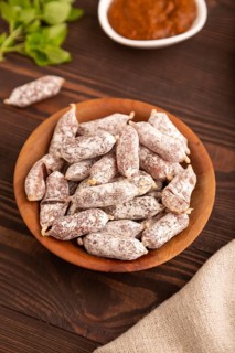 Small smoked Chicken sausages in wooden bowl on brown wooden background and linen textile. side