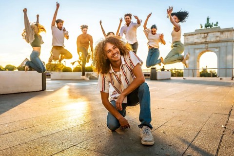 Free style dancer kneeling smiling at camera supporting by multi-ethnic friends jumping on the