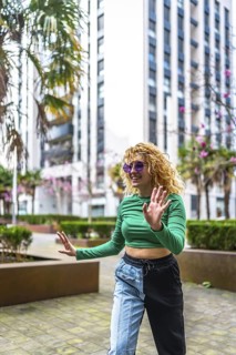 Energetic young woman with curly hair dancing in a modern city setting, surrounded by tall