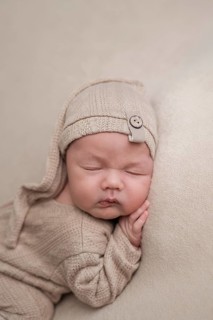 A serene newborn baby peacefully sleeps while dressed in a soft, beige knit outfit, complemented by