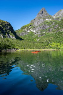 Two kayakers with red kayaks in the fjord Trollfjord, mountain peaks are reflected in the water,