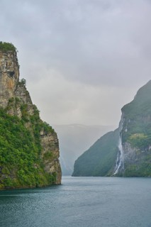Geiranger Fjord with waterfall surrounded by rocks and mountains with overcast sky, Geiranger,