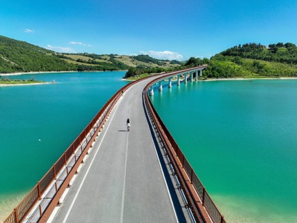 A young woman walks alone on a picturesque bridge surrounded by lush greenery and turquoise waters