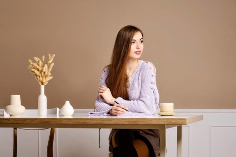 Young cheerful woman writing letter sitting behind the table at home