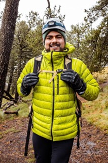 A hiker wearing bright green gear navigates a muddy, rain-soaked trail through a dense forest.