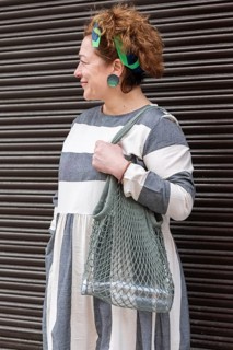 A woman in a stylish, grey and white striped dress stands confidently with her eco friendly mesh