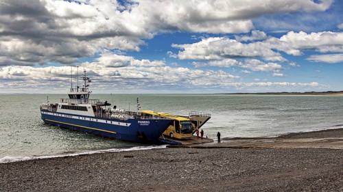 Ferry on a pebble beach in front of a cloudy sky and calm sea, ready for departure, The car ferry
