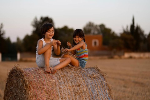 A joyful scene in a rustic field where two young kids, a boy and a girl, play on a large hay bale.