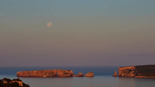 The moon is high above rocks and calm water, the sky is pink, Tsichli Baba island, Sfaktiria