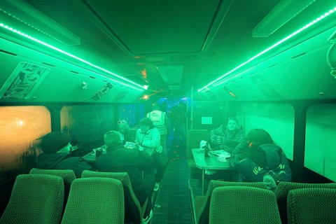 Interior view of a bus with green lighting, in which several people are sitting at tables,