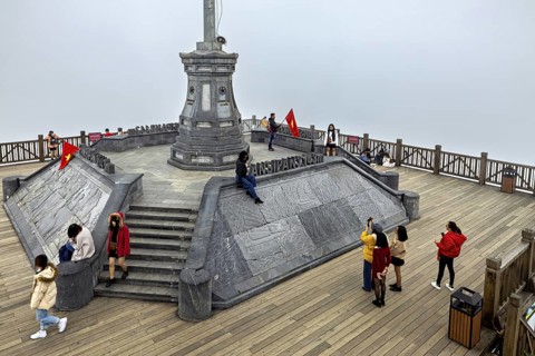 People on a platform in the mist, surrounded by railings and a flag. Stone structure with steps in